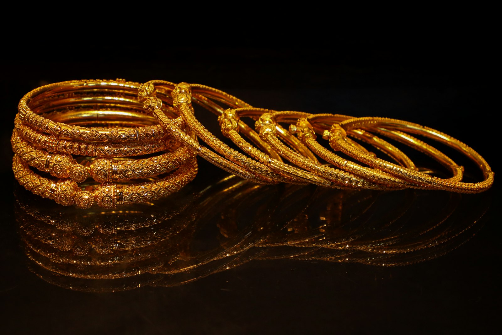 A stack of ornate gold bangles on a dark surface